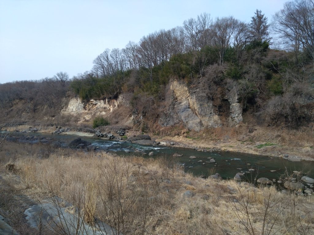 千曲川沿いに切り立つ岩壁と、川の流れに沿って続く早春の道。