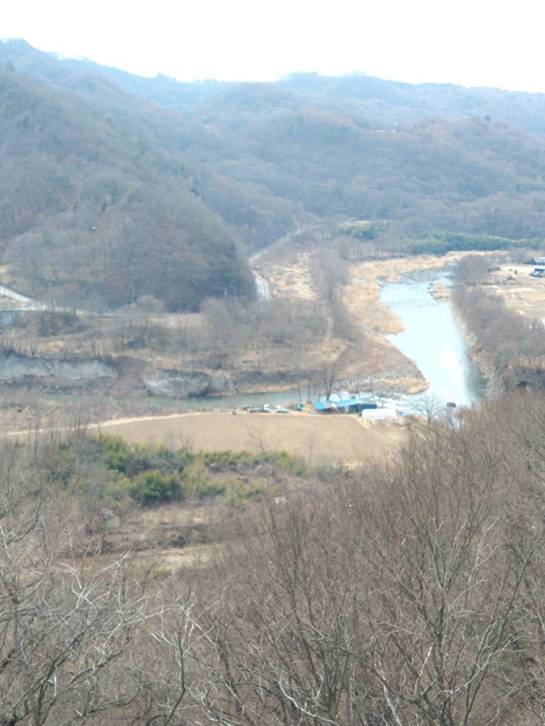 高い場所から見下ろした千曲川と川沿いの畑、早春の山並みが広がっている。