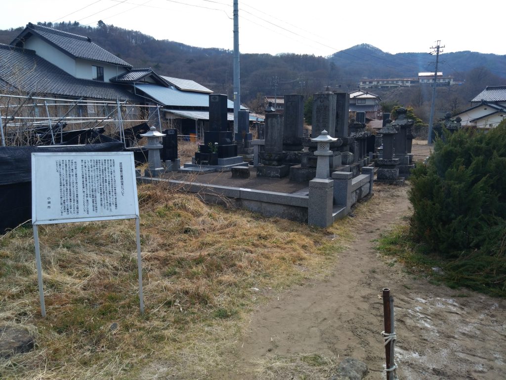小諸市の案内板の前に、武田信繁の墓所と周囲の墓石群が静かに並んでいる。